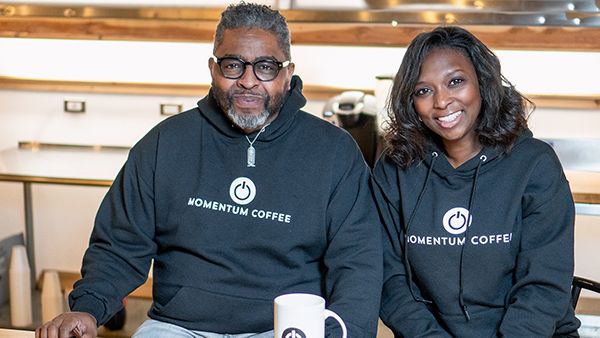 Tracy Powell and Nikki Bravo sit for a portrait in sweatshirts branded with Momentum Coffee