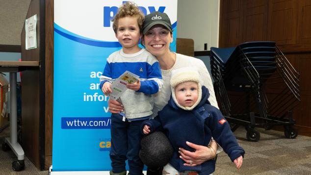 Family that includes mother and two toddlers in front of the WTTW Kids Learn & Play banner
