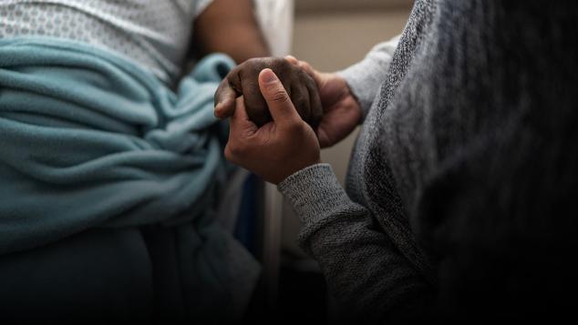 The hand of a medical patient in hospital gown is being held by another person
