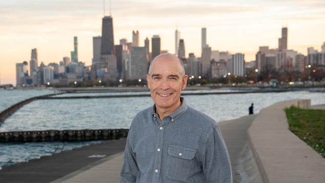 Geoffrey Baer stands along Lake Michigan lakeshore with the city of Chicago in the background