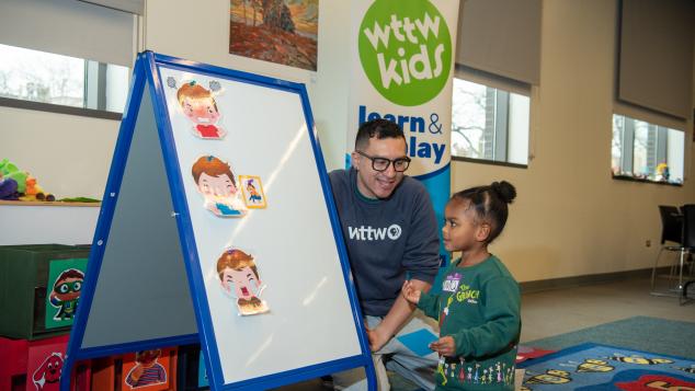 WTTW Kids Learn & Play host Cristian engages with child in front of a easel.