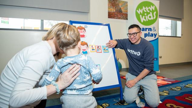 WTTW Kids Learn & Play host Cristian engages with a toddler in front of an easel. 