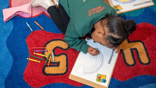 Young girl is coloring a rainbow in a coloring book at WTTW Kids Learn & Play