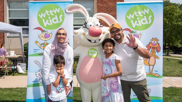 A family of four poses with Nature Cat in front of two WTTW Kids banners