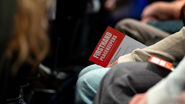 Closeup of audience members seated holding FIRSTHAND: Peacekeepers brochure