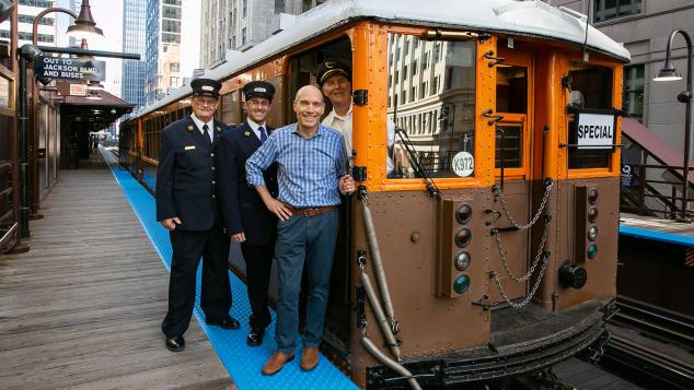 WTTW's Geoffrey Baer and three CTA train conductors stand next to a vintage 1920s Chicago L car