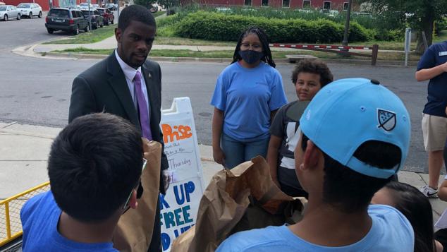 A group of young people gathered around a young man in businees attire who is speaking