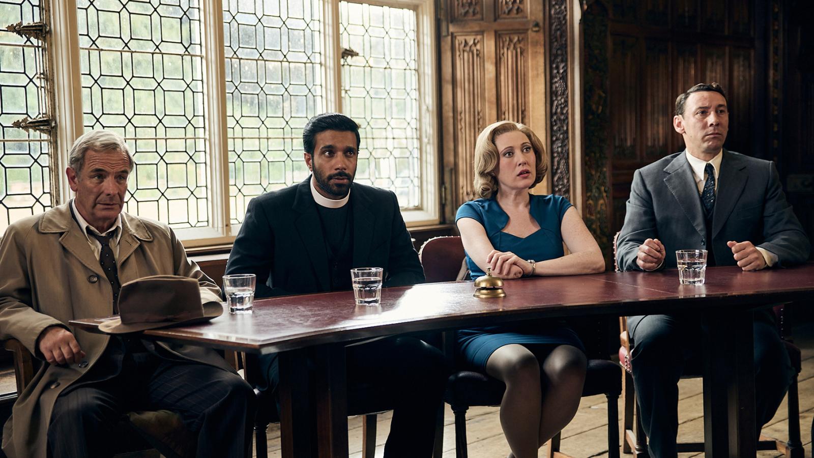 Geordie, Alphy, Miss Scott, and Leonard sit behind a table in an ornate hall