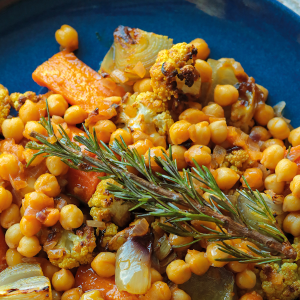 A blue plate of chickpea stew with vegetables topped with a sprig of rosemary