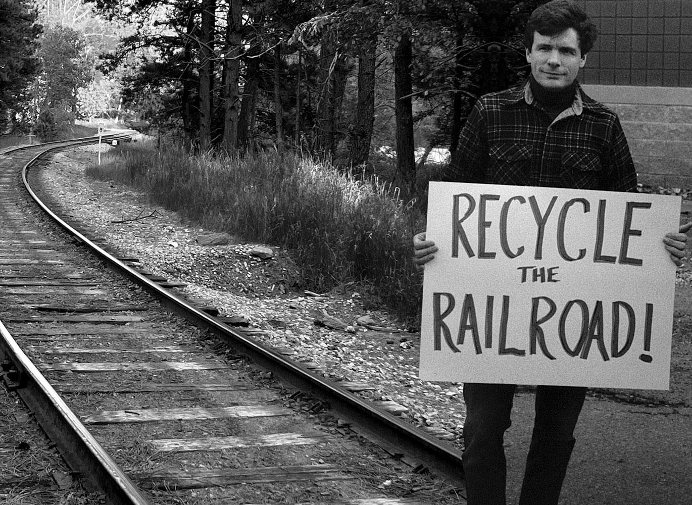 Man near tracks with sign that reads Recycle the Railroad Man near tracks with sign that reads Recycle the Railroad