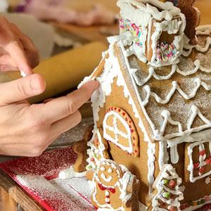 Hands creating a gingerbread house.