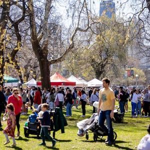 People walk on a lawn in a park where a farmers market is taking place