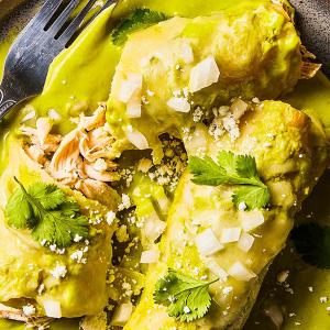 Enchiladas on a plate drenched in cheese and green sauce