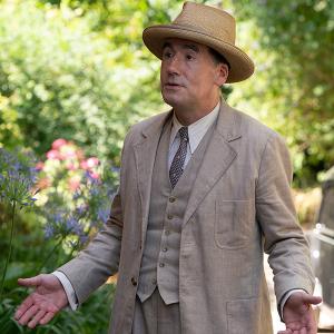 Atticus Pund stands in a hat and light suit outside with his arms spread