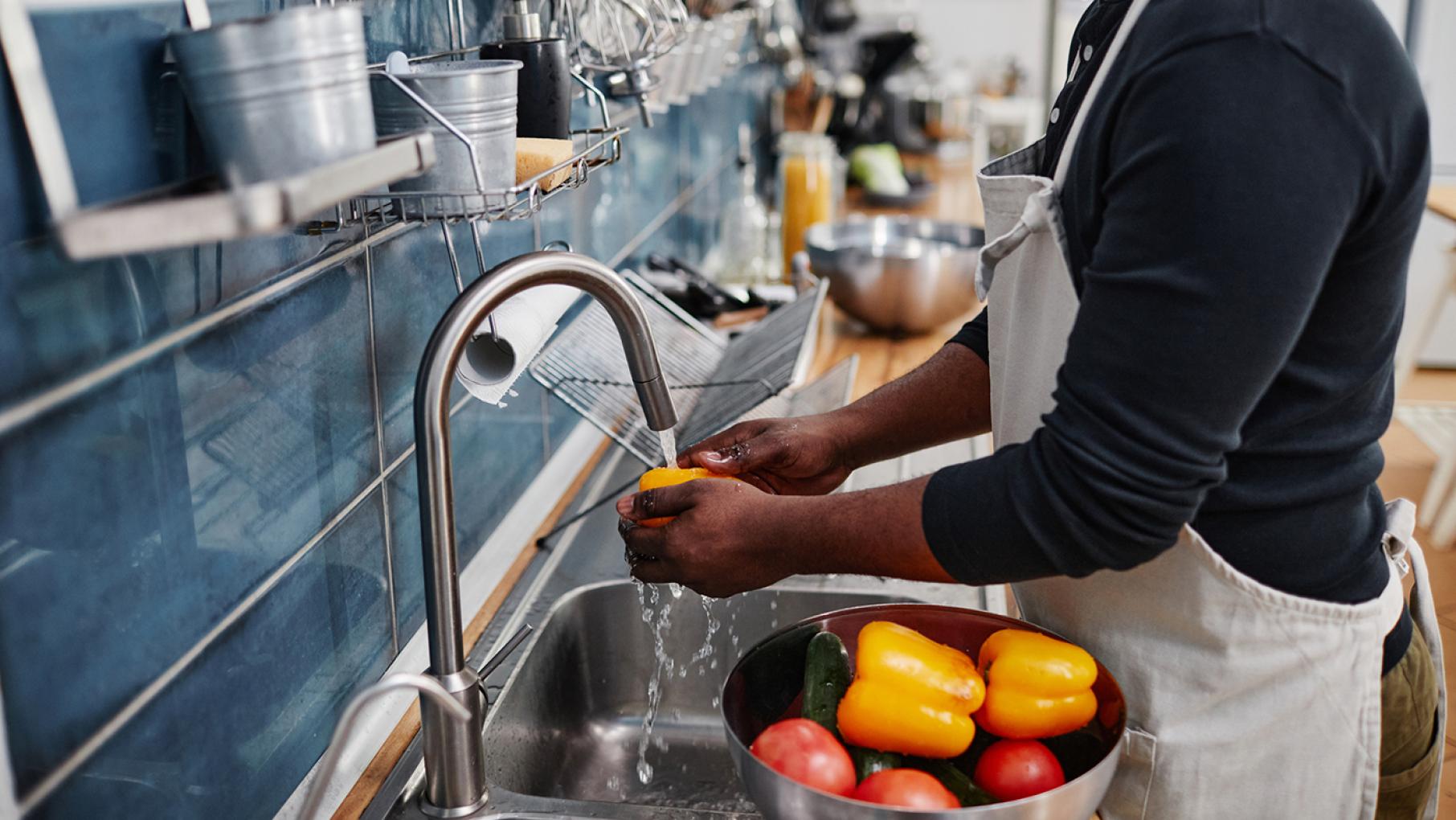 A man washing bell peppers in a restaurant kitchen