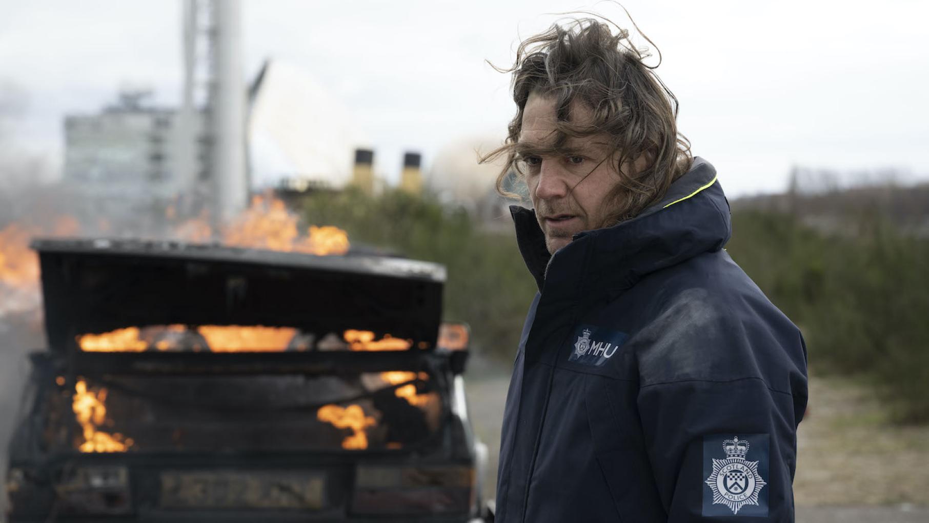 Micahel is uncomfortably close to the team's latest case. Photo: UKTV Michael by Annika's burning car