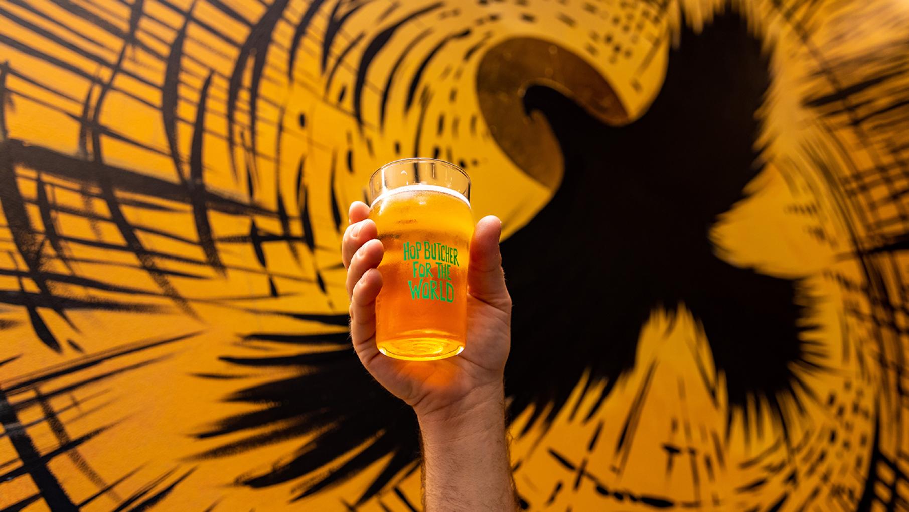 A hand holding up a Hop Butcher beer in a glass