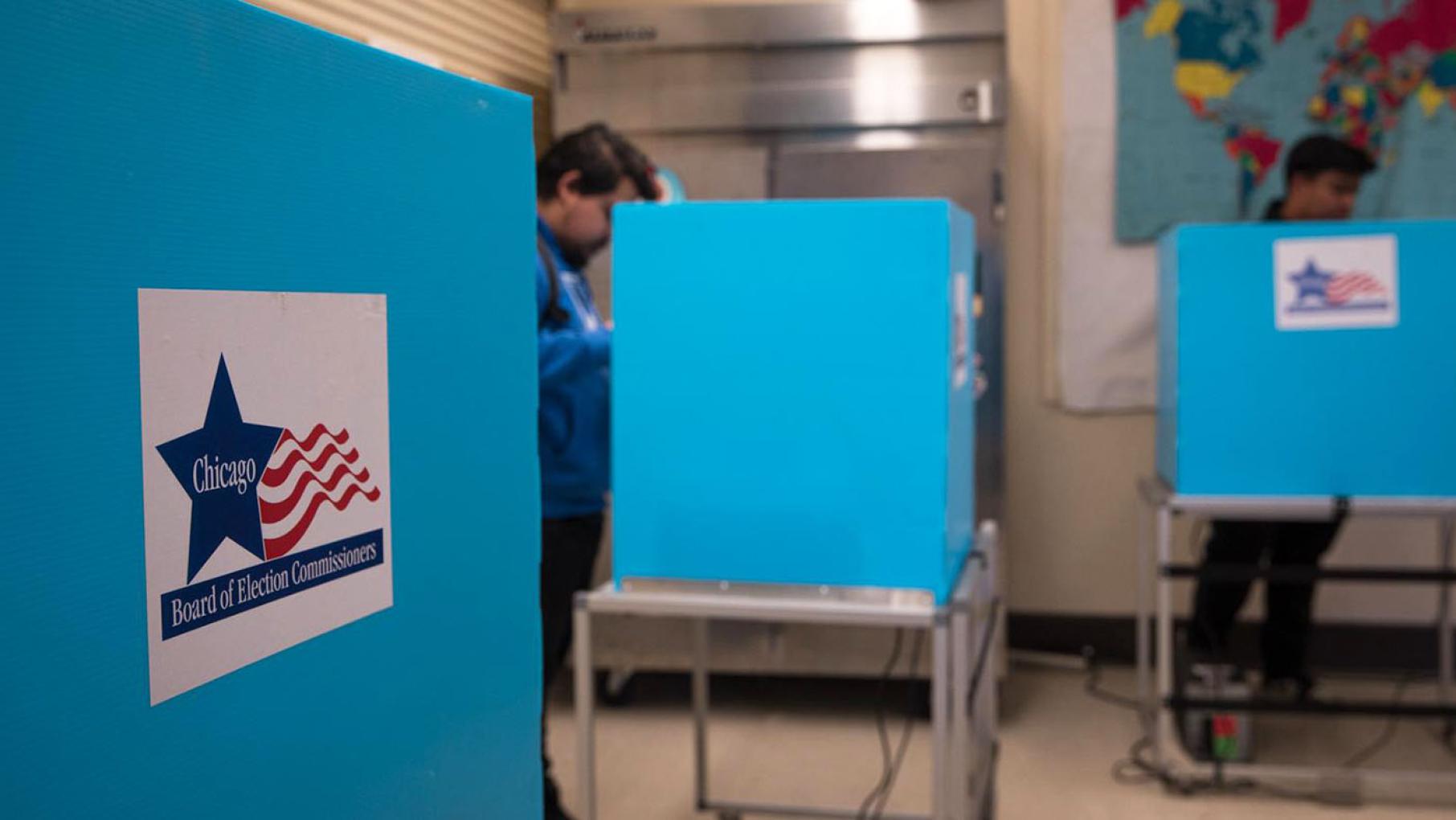 Two seniors from Kelvyn Park High School fill out their ballots for the Feb. 28 Chicago municipal election behind voting booths at the Kilbourn Park polling station. (Michael Izquierdo / WTTW News)