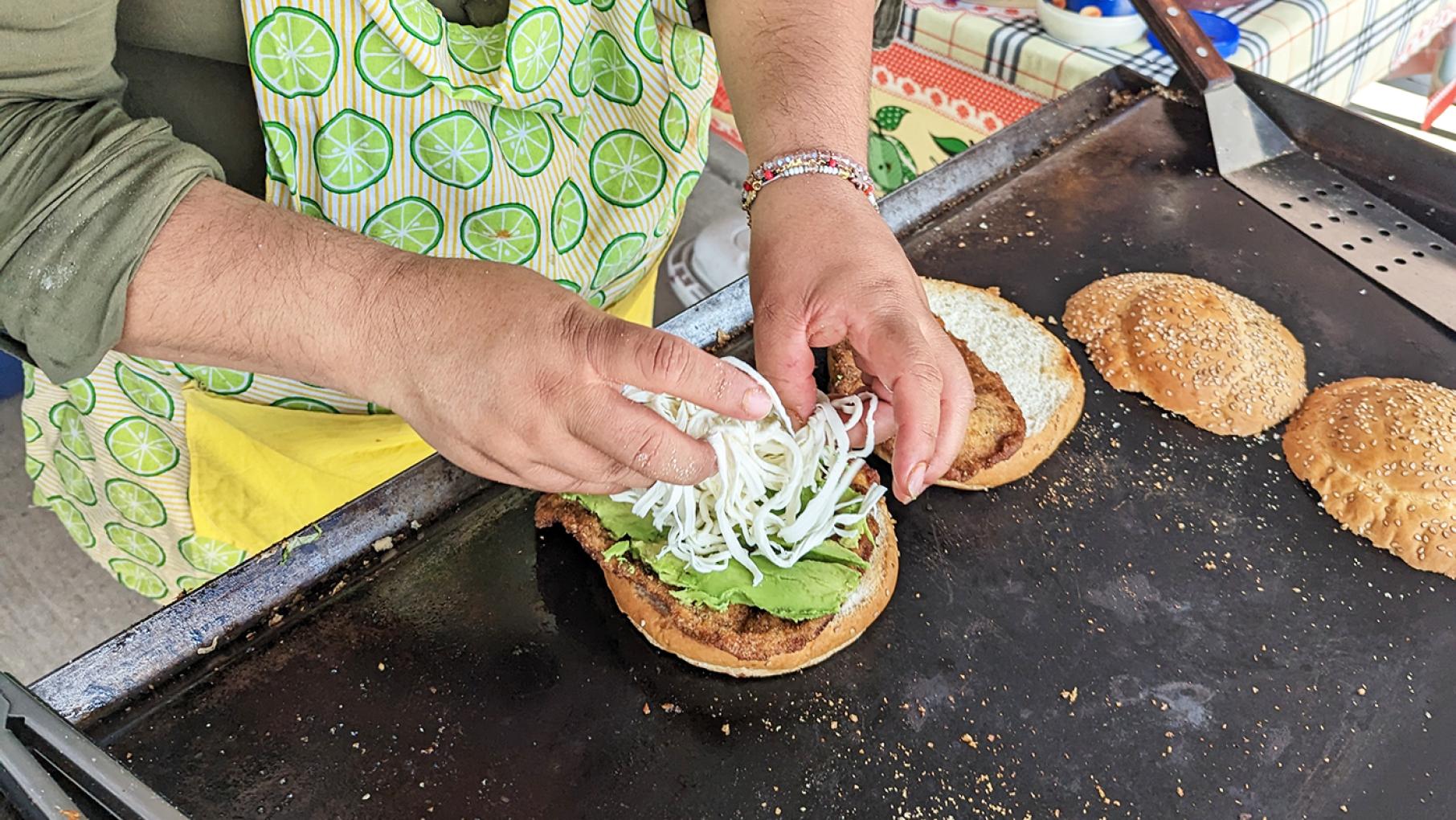 At a food stall at the Swap-O-Rama flea market in Back of the Yards, Maria prepares a cemita poblana. Image: Lisa Futterman A woman's hands shown preparing a cemita