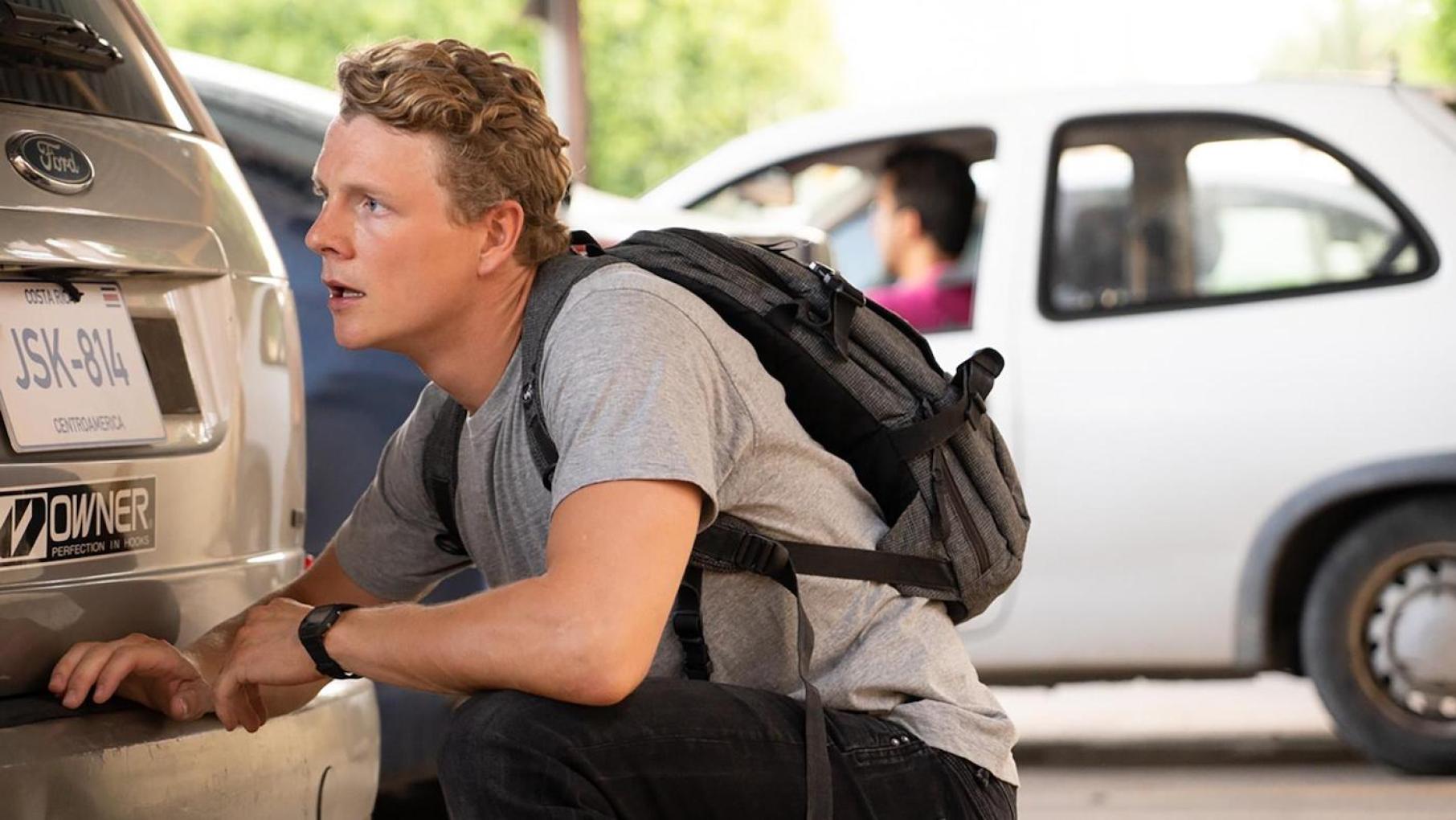 Christian squats behind a car in Before We Die