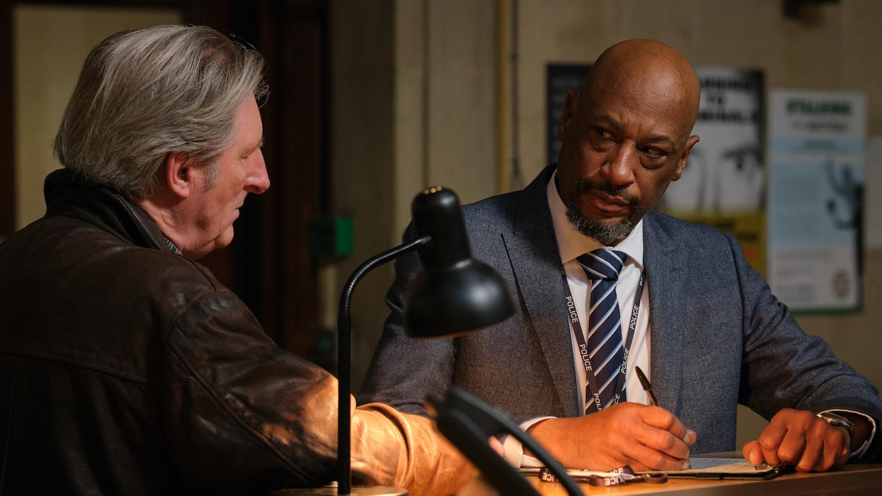 Ridley and Goodwin sit at a desk together with a desk lamp illuminating it