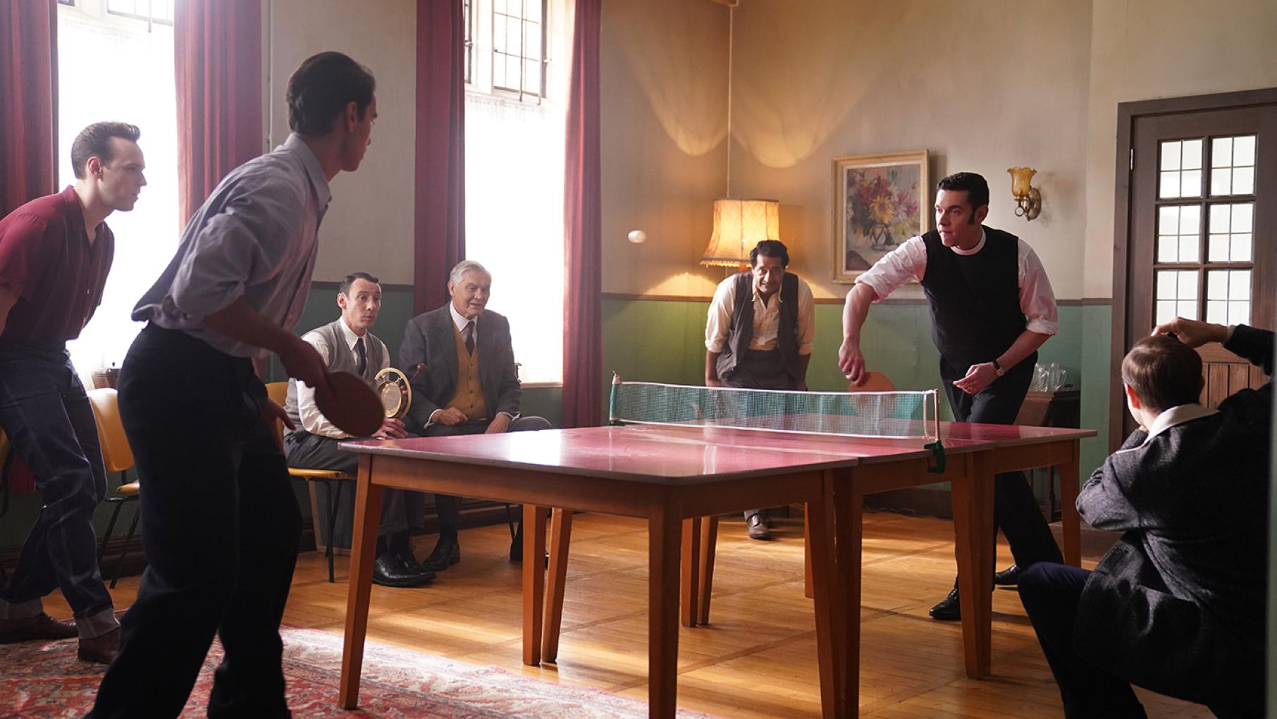 Will plays table tennis with a man while others cheer on the game