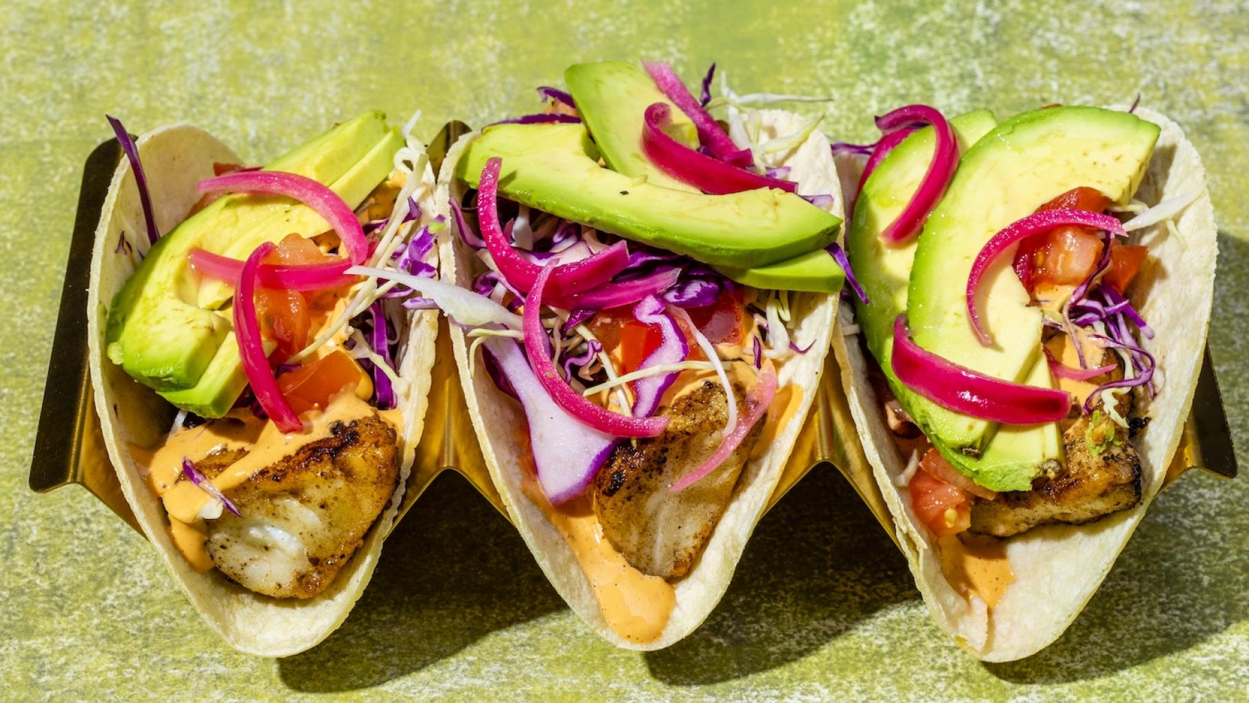 These fish tacos are inspired by a version at a San Diego restaurant. Photo: Cook's Country Three fish tacos with avocado and pickled red onion and slaw in a stand