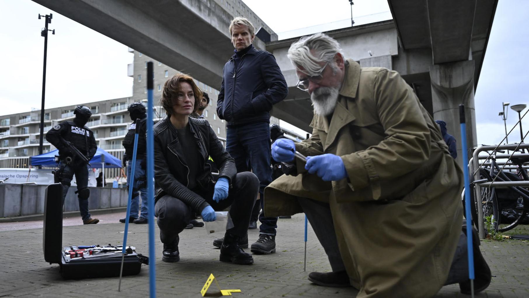 A freerunning champion is shot and killed while driving. Photo: Company Pictures, NL Films & A3MI Hendrik squats and works on a crime scene while Lucienne squats behind him and Van der Valk stands