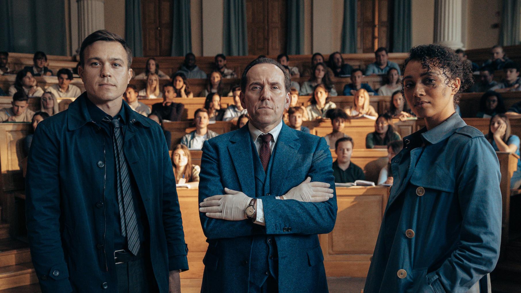 Dan, Professor T, and Lisa stand facing the camera in a lecture hall full of students