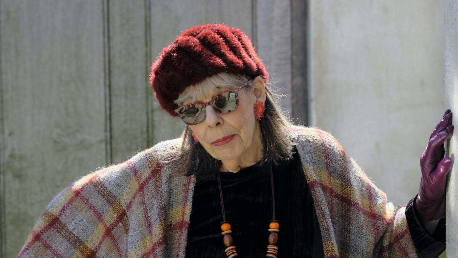 Adelaide stands in a red hat and sunglasses with her arm against a wall