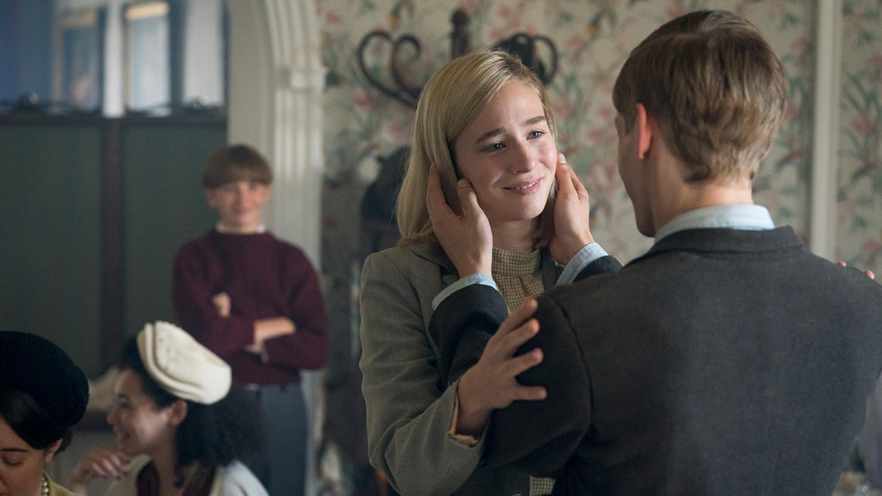 Gregor holds Kasia's face while she holds his arms, smiling, with Jan in the backgronund