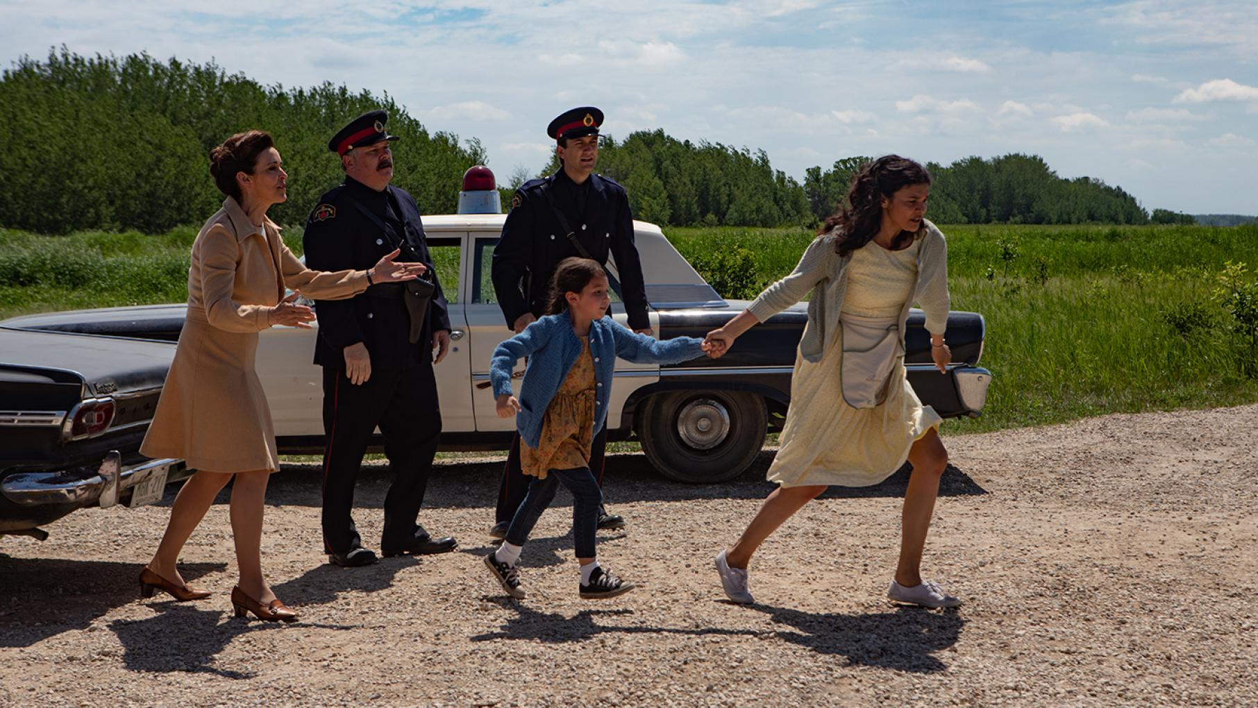 Patricia grabs her daughter by the hand to run away from a woman and two policemen standing in front of a police car