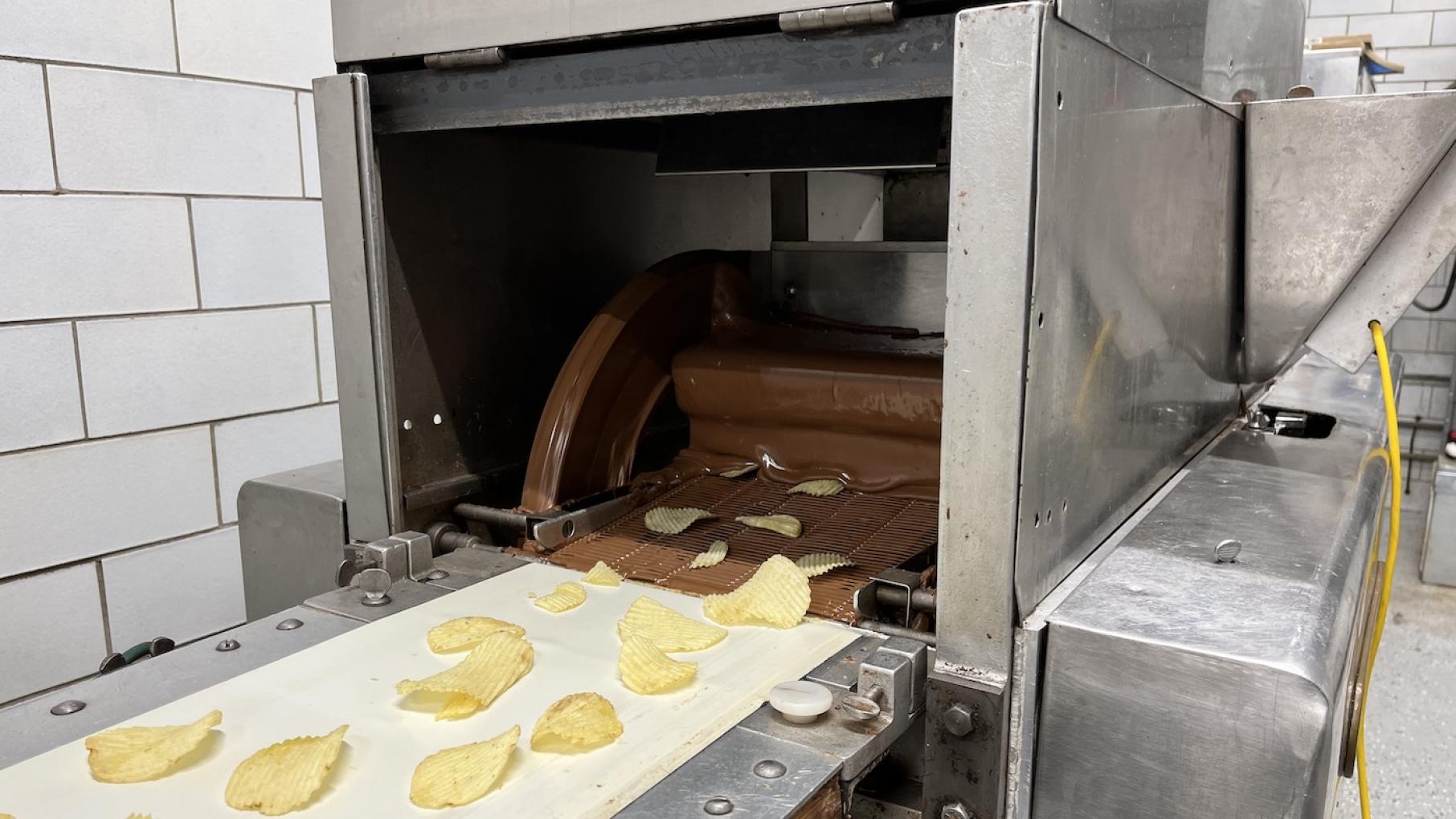At the old Cupid Candies factory in Chicago, Stephanie Hart produces goodies like chocolate-covered potato chips under the name Life is Sweet Potato chips on a conveyor belt going through a curtain of liquid chocolate