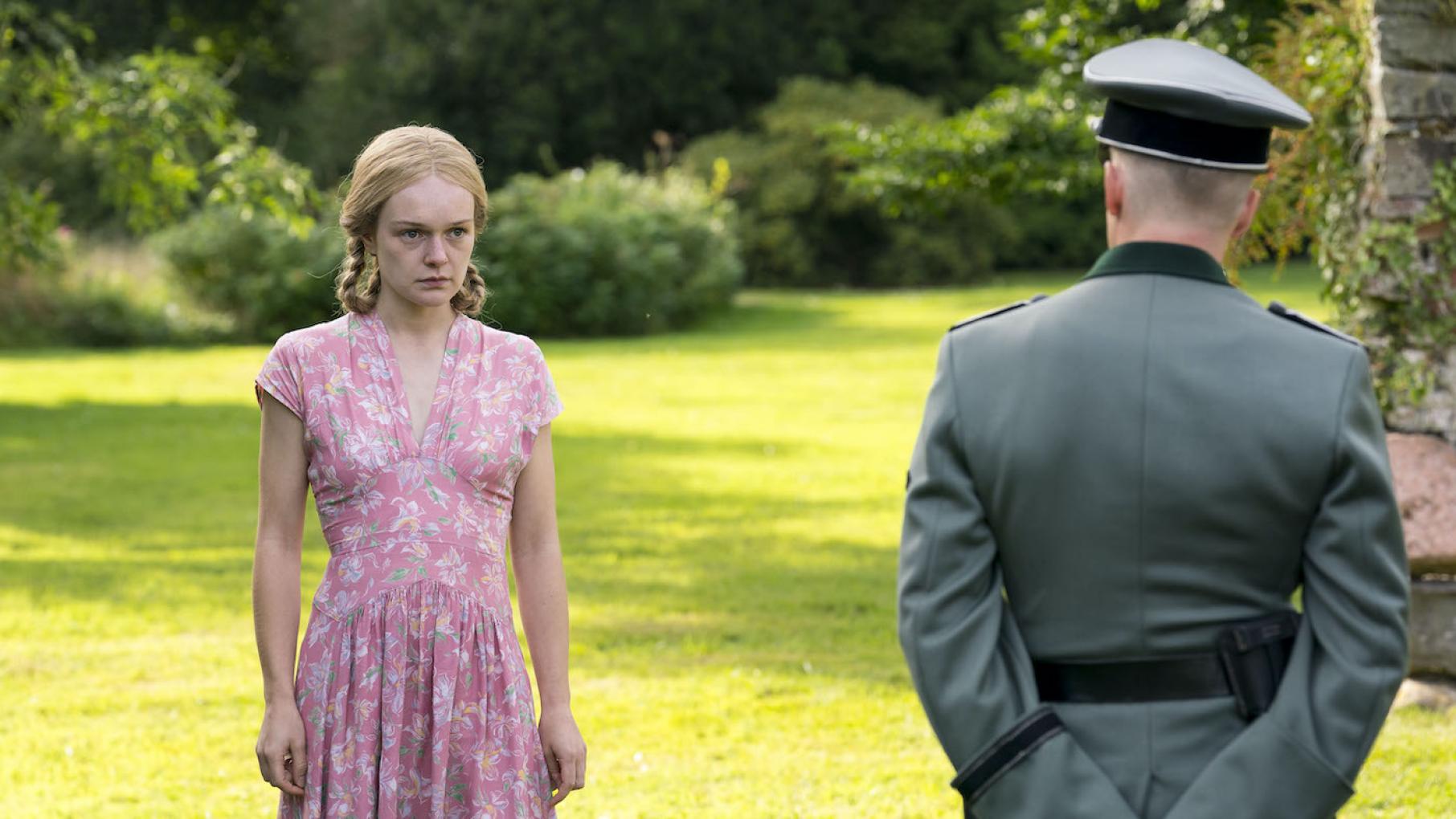 Marga begins to experience what it means to devote herself to the Reich. Credit: Mammoth Screen. Photo by Steffan Hill Marga stands on a lawn in a pink dress and looks uncertainly at a German officer eying her