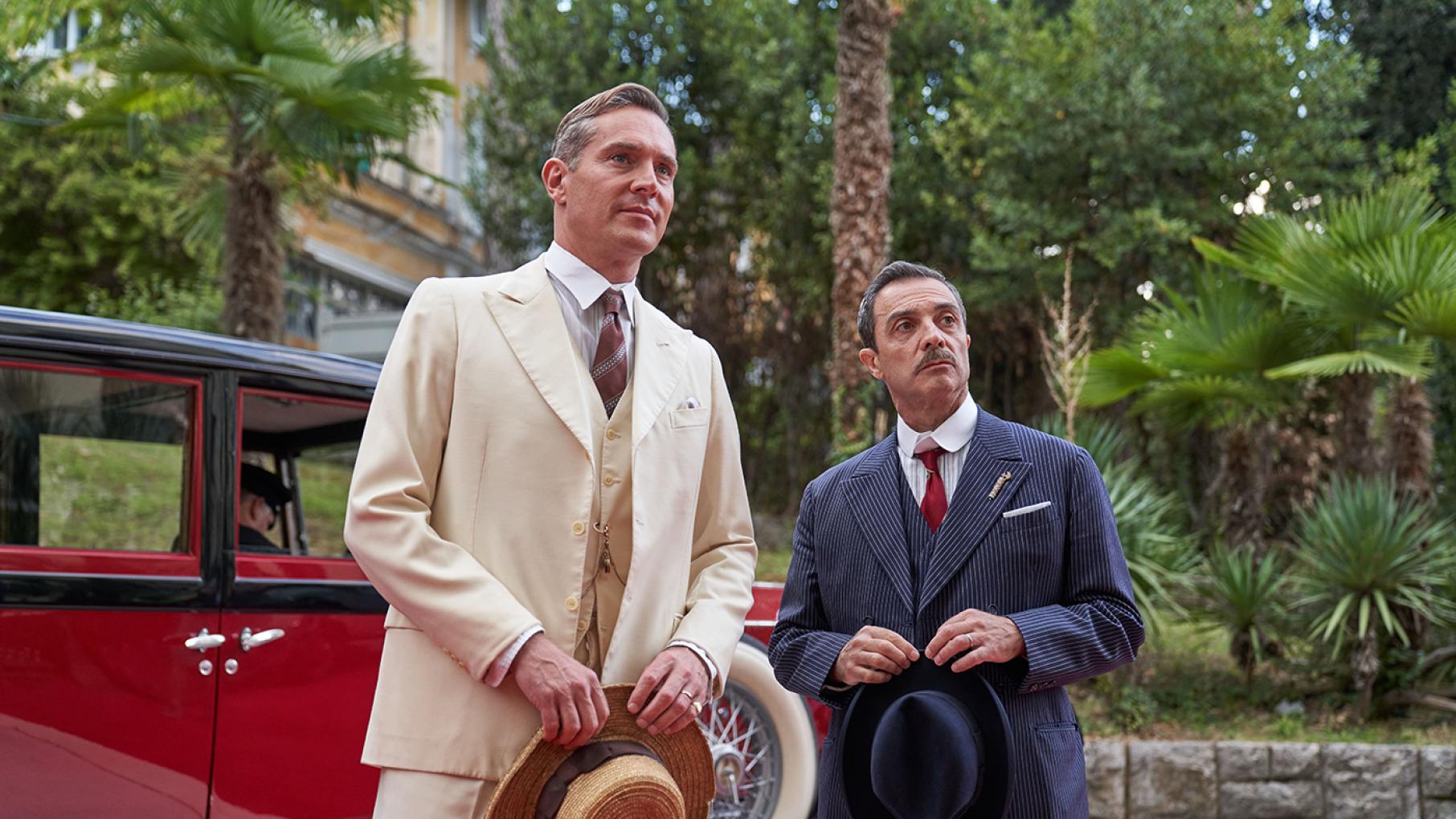 Cecil and Danioni stand in front of a red car, looking toward something