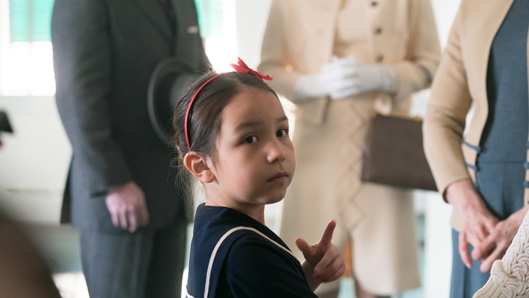 Bezhig in front of well-dressed adults, with a bow in her hair