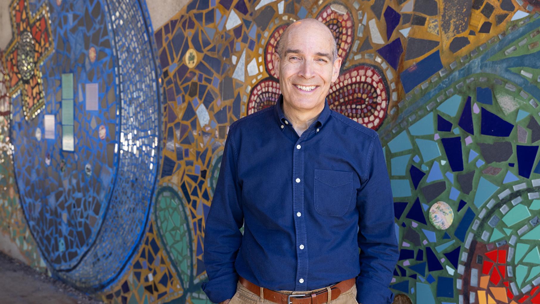 Geoffrey Baer is back to discover more of 'The Most Beautiful Places in Chicago.' Credit: Kristan Lieb Geoffrey Baer smiles in front of a colorful mosaic mural