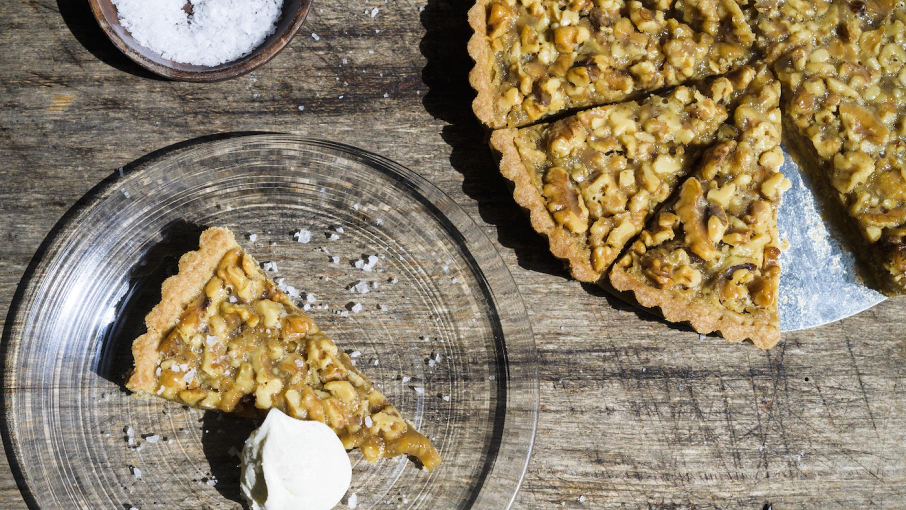 A French walnut tart cut into slices, with a slice on a plate with cream