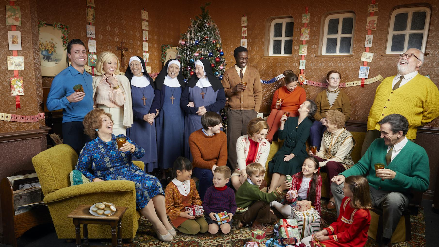 The cast of Call the Midwife all smile and laugh in front of a Christmas tree