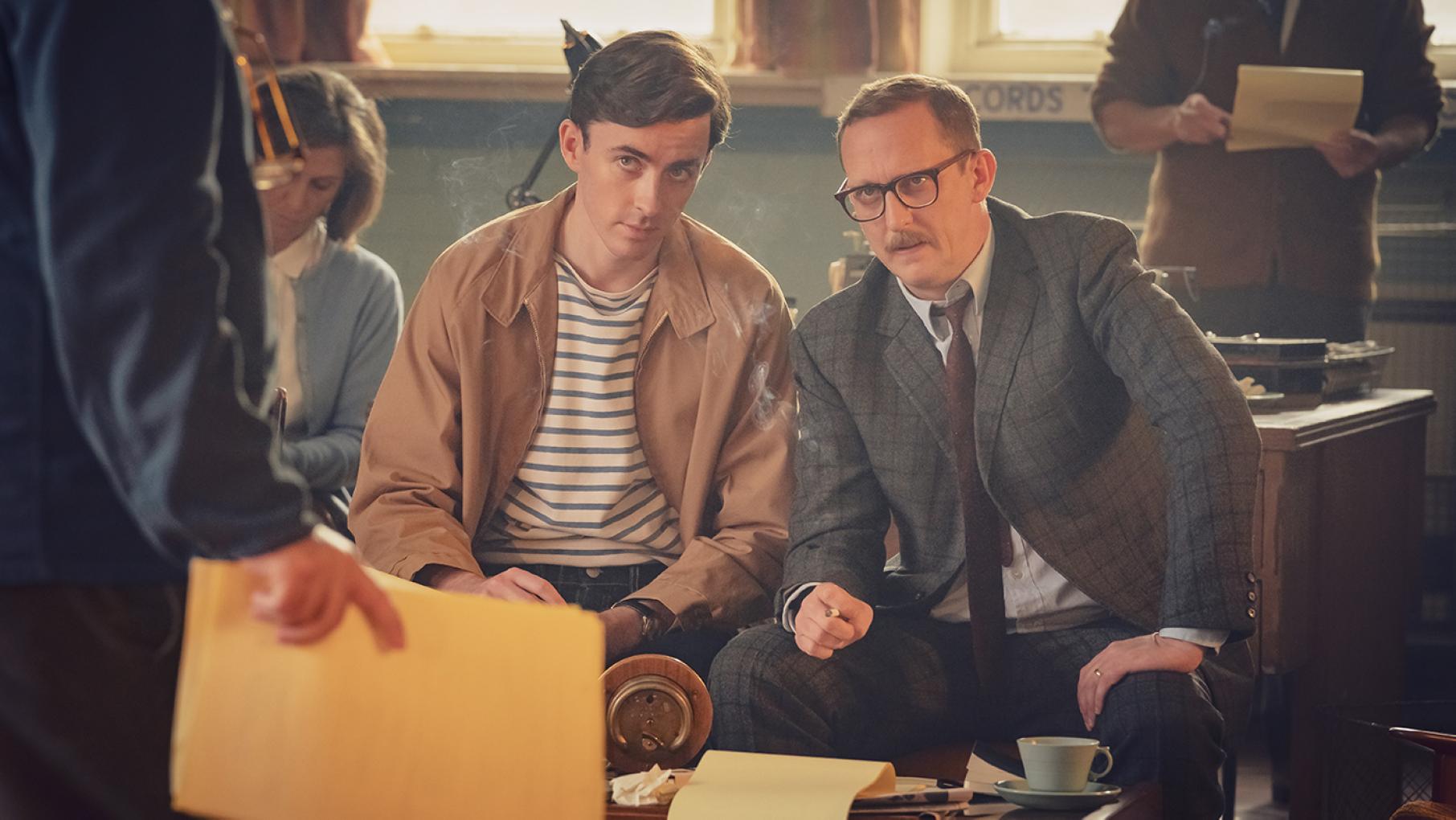 Two writers sit and look skeptically at someone standing in front of them