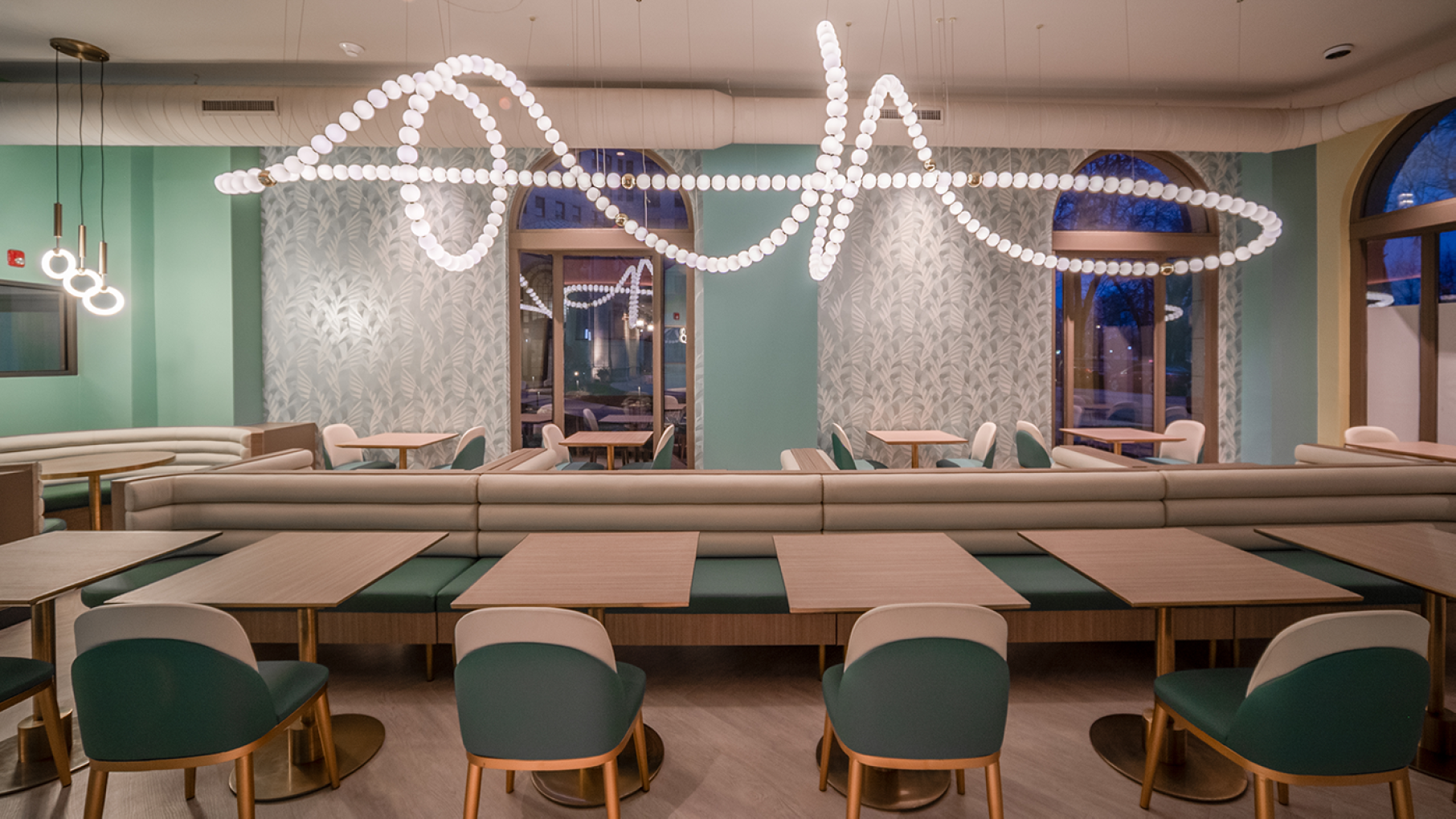 The interior of a restaurant, with a squiggly, abstract light fixture above tables and booths