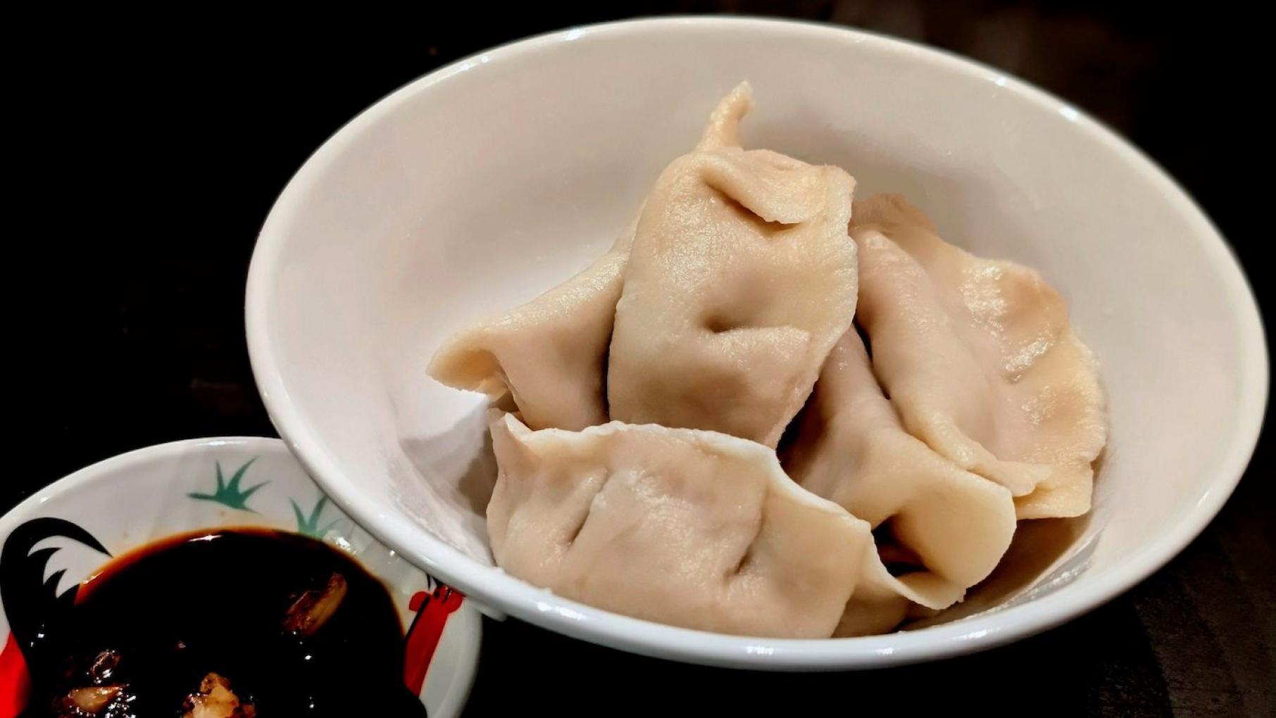Jiaozi are often served at Chinese New Year in the hope that they bring prosperity because of their resemblance to ancient currency. Credit: Courtesy Rich Wang Chinese dumplings in a white bowl next to a smaller bowl of dipping sauce