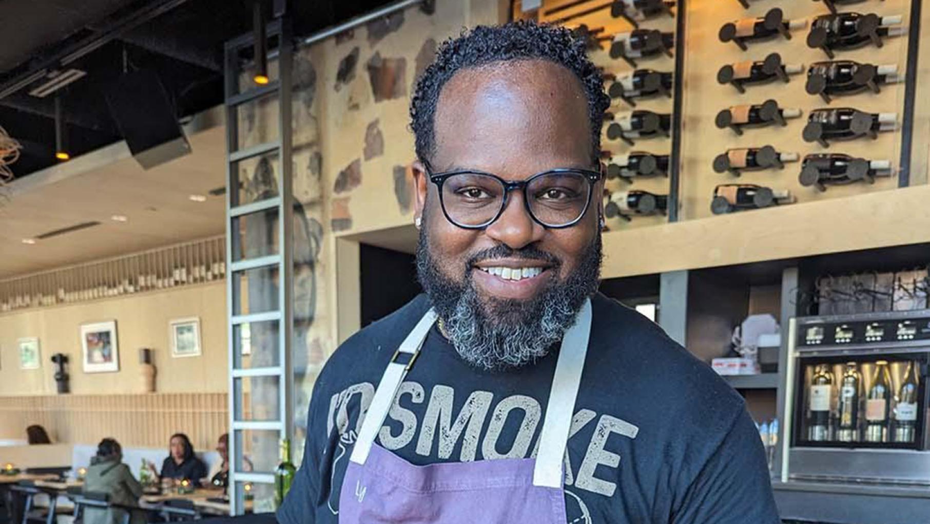 Bronzeville Winery, with food by chef Lamar Moore, is one of the restaurants taking part in Chicago BLACK Restaurant Week. Credit: Lisa Futterman for WTTW Lamar Moore smiles at Bronzeville Winery in a purple apron