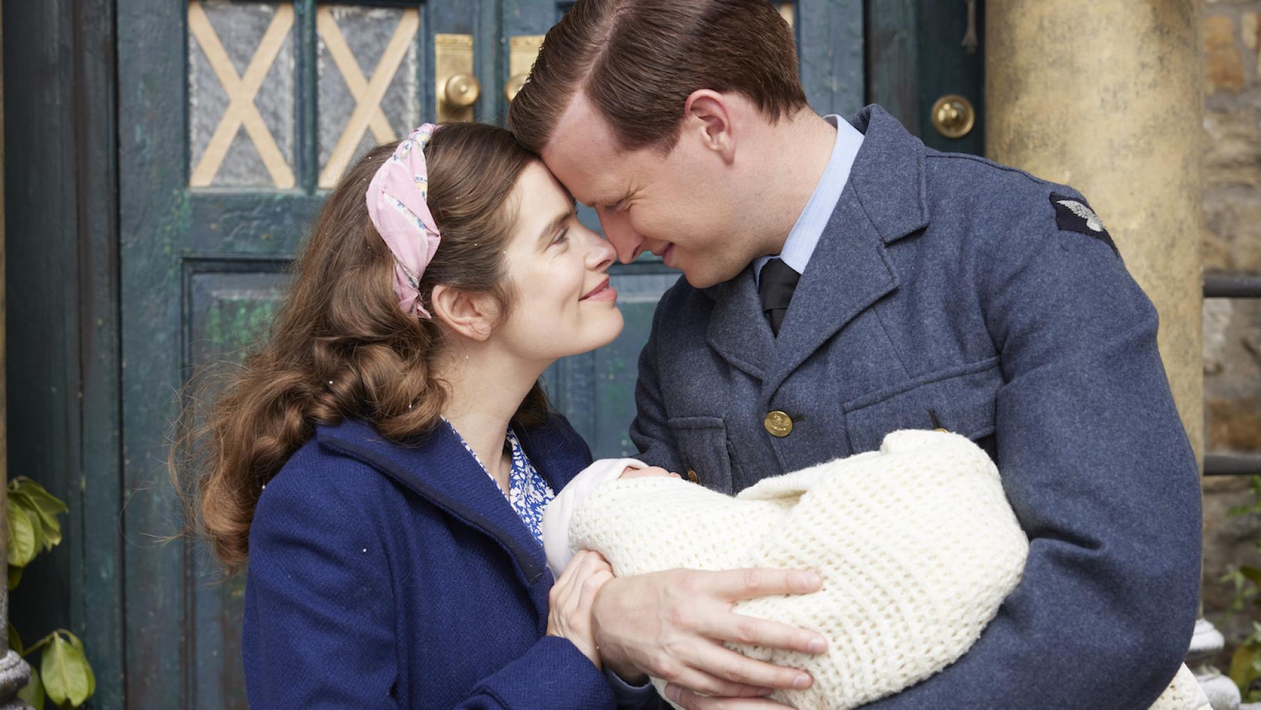 Helen and James smile and hold their heads to each other as James holds their newborn