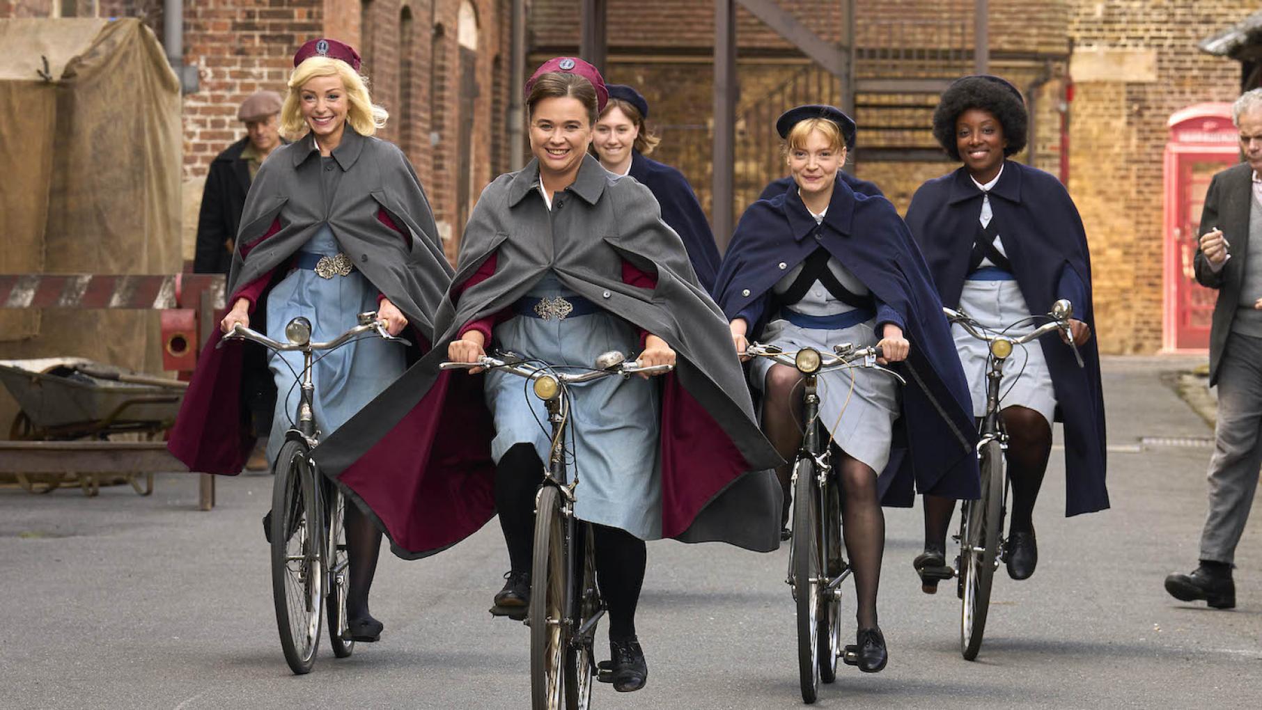 The midwives and their pupils ride bikes down the street, smiling in their uniforms 