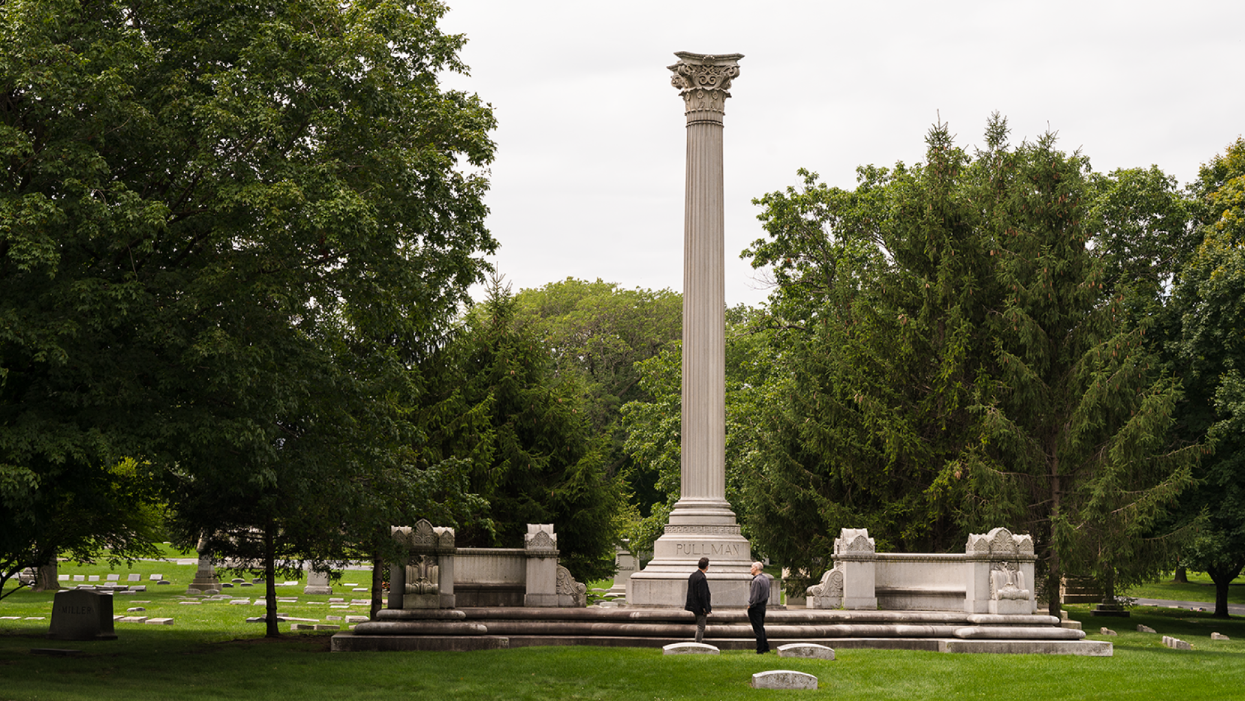 George Pullman is rumored to be buried under lots of steel and concrete in Graceland Cemetery so his body wouldn't be desecrated by angry workers. Credit: Ken Carl for WTTW Two men stand in front of a column that is part of a memorial in a cemetery