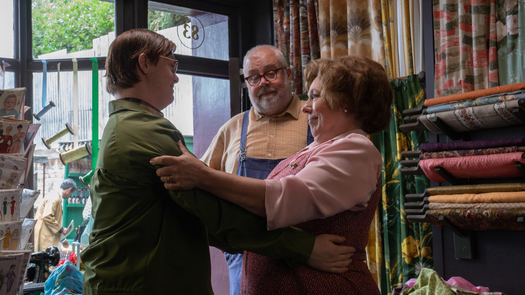 Reggie and Violet hold each other while Fred looks on in their shop