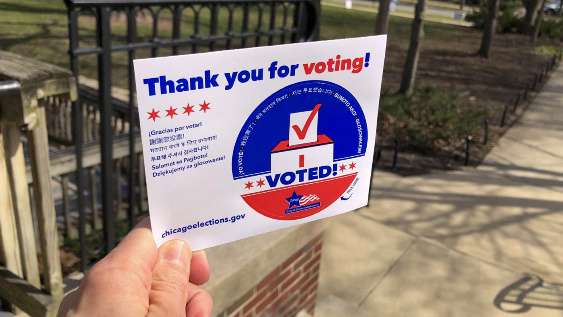 A hand holding up an "I Voted" sticker