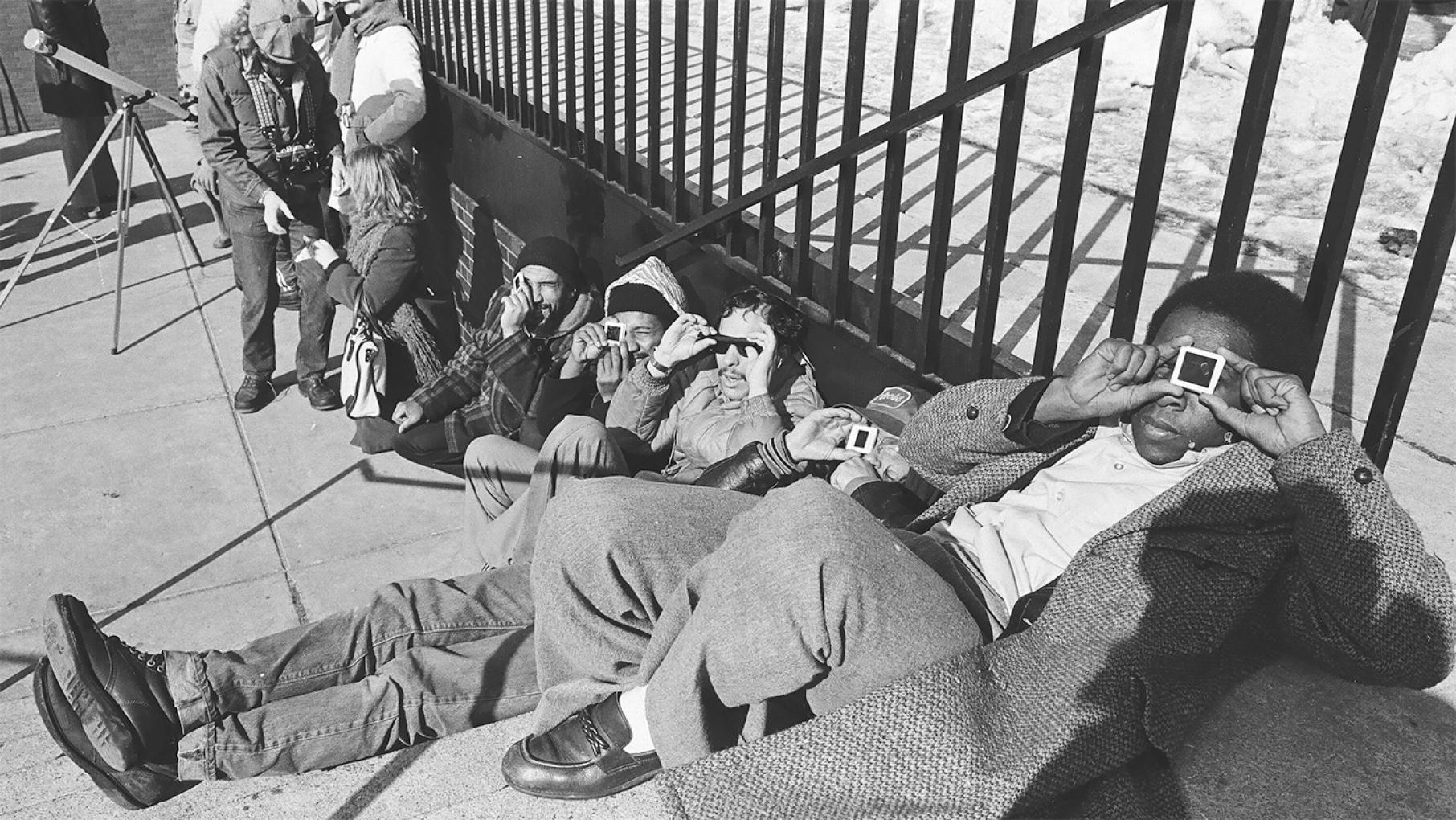Eclipse viewers at Adler Planetarium in 1979. Credit: ST-14001507-0002, Chicago Sun-Times collection, Chicago History Museum A black and white image of eclipse viewers sitting on the ground and viewing the eclipse through viewing devices at Adler Planetarium in 1979.