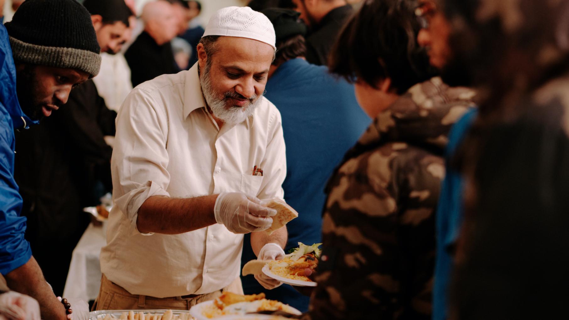 Fasting is an integral part of Ramadan, as is charity and doing good deeds. Credit: Jack X. Li for WTTW A man in plastic gloves puts pieces of pita on the plate of a person in line